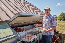 Dennis Hartmann vor seinem mobilen Hühnerstall. (Nachhaltigkeits-Projekt: Legehennenhaltung Hartmann)