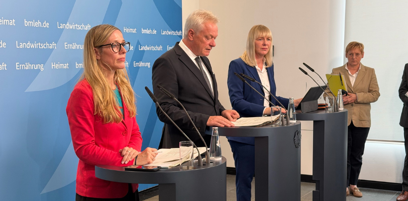 m Vordergrund stehen drei Personen hinter Pulten, die mit Mikrofonen ausgestattet sind. Die mittlere Person trägt einen dunklen Anzug und hält ein Manuskript, während die beiden anderen Personen links und rechts jeweils einen farbigen Blazer tragen. Im Hintergrund befindet sich eine weitere Person mit Tablet. Die Wand hinter den Pulten zeigt das Logo und die Schriftzüge des Bundesministeriums für Ernährung und Landwirtschaft. Die Szene vermittelt den Eindruck einer Pressekonferenz zum Erntebericht, bei der Alois Rainer und Nikola Steinbock im Mittelpunkt stehen.